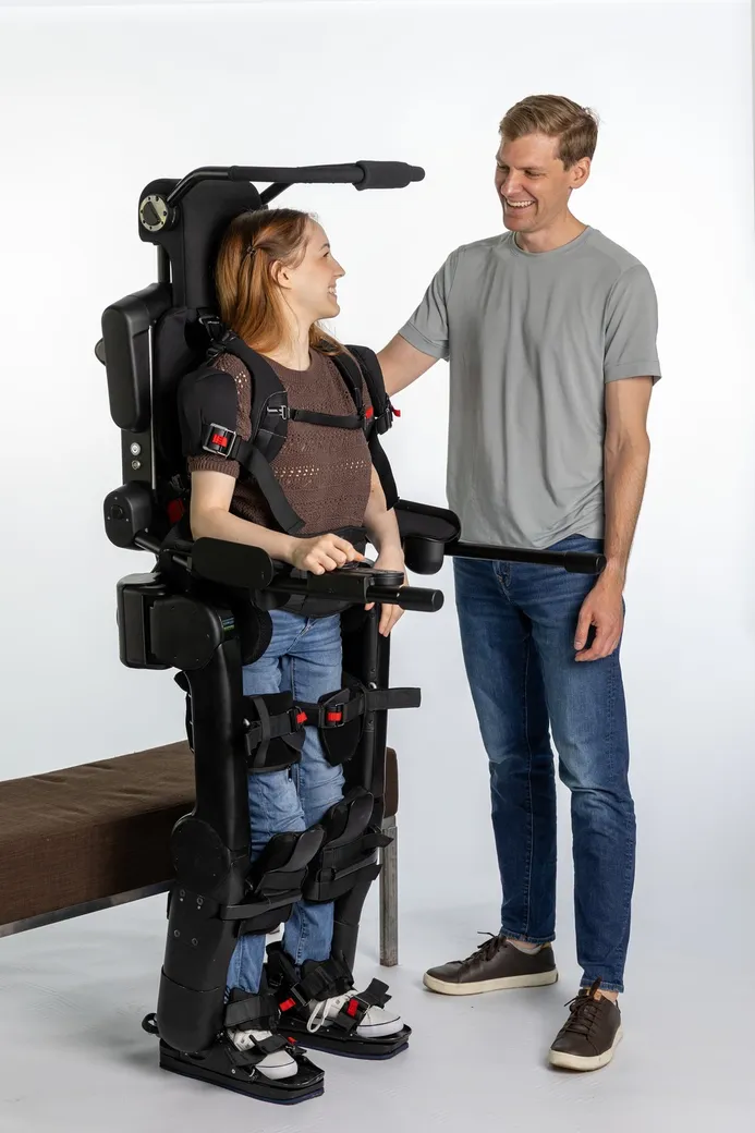 Utilisatrice de l'exosquelette Wandercraft Eve, manette en main, avec son accompagnant à portée de bras